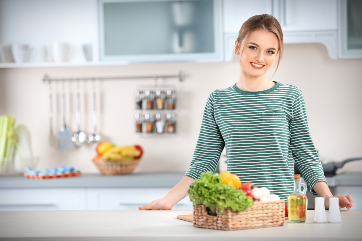 Young kitchen. Корзинка овощи и девушка в кухне фото.